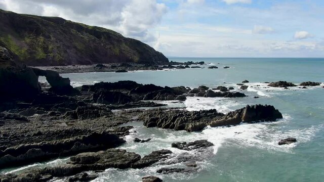 Aerial shot of the waves in the sea and the rocks and hillside at Spekes Mill coastal beach in Devon