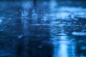 a blue scene of wet reflection floor from heavy raining with splashing water from rain droplet, photograph shot with very shallow depth of field focusing