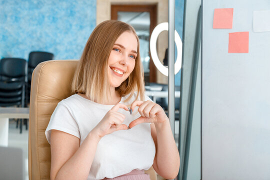 Young woman blogger records live video content, broadcasts live to subscribers shows like heart sign using mobile phone and ring light lamp. Vlogger influencer ternager girl smiles speaks to camera