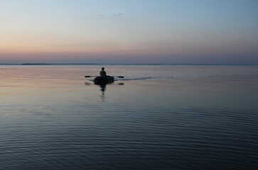 Russia, Novosibirsk 06.07.2019: male fisherman on a boat with oars sea at sunset dawn on the waves