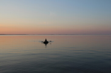 Fototapeta premium Russia, Novosibirsk 06.07.2019: male fisherman on a boat in the sea at sunset dawn on the waves