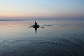 Russia, Novosibirsk 06.07.2019: male fisherman on a boat with oars sea at sunset dawn on the waves