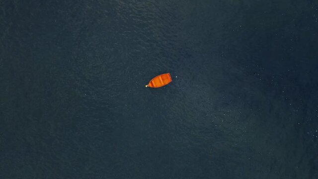 Drone shot above small red wooden boat tracking and spinning towards it with vast open water around the boat