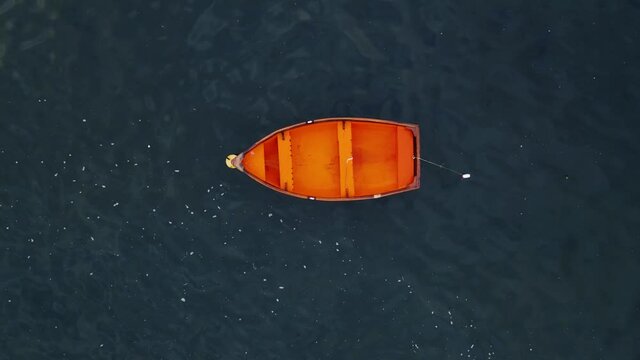 Drone shot flying upwards from a small red boat in the middle of the ocean with no one inside it