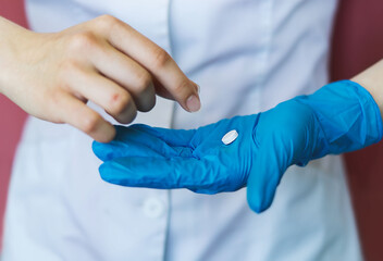 The doctor's hand, a nurse in a blue latex glove gives a pill in the palm of a sick patient. A blurry hand takes the medicine. The concept of medical care, speedy recovery