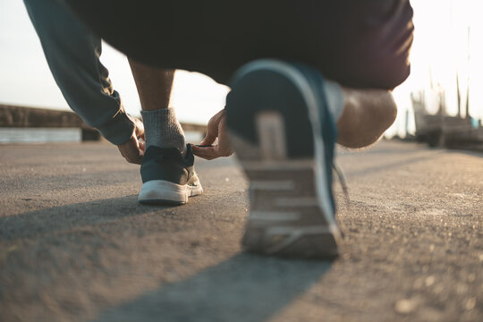 closeup of man tying shoe laces on the road before running in sunset. Sport and workout concept.