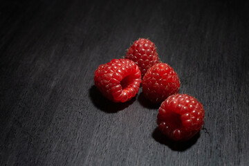 four red fresh raspberries on a black wooden background