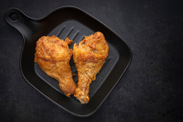 heart shape of crispy fried chicken drumstick in black pan on the dark tone texture background with copy space for text, top view shot