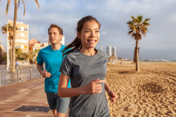 City morninig run happy fit couple runners running on Barcelona beach. Smiling youn Asian woman training cardio exercising jogging. - Powered by Adobe