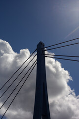 La flèche d´un pont piéton sur fond de ciel bleu et de nuages blancs, un rayon de soleil arrive sur la droite.