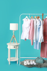 Rack with stylish clothes, accessories and table on color background