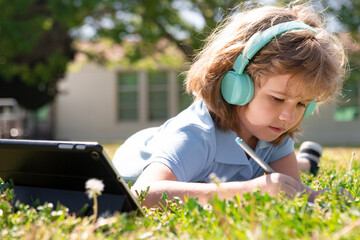 On line kid learning in school park. Portrait of a schoolboy pupil lying on the grass with a book outside.