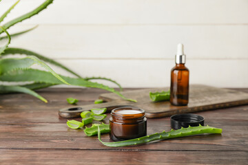 Jar with cream, bottle of essential oil and aloe pieces on wooden background