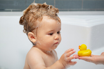 Little baby child is washing her hair in bath. Child bubble bath.