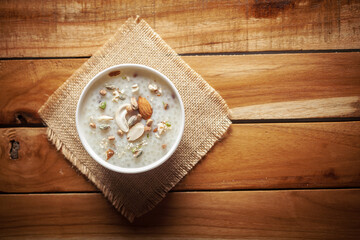 Close-up of Creamy Sabudana Kheer Garnished with dry fruits. Indian delicious dessert. Served in the white ceramic bowl. Top View on wooden background and jute mat.
