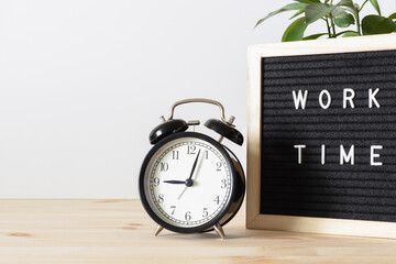 Classic black alarm clock on wooden table and black board with words 'work time' with white wall background and copy space.