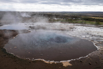 Landscape with geothermal pool with deposits of silica in the edges with ecoins throw in by tourists, at Geysir geysers in Iceland