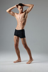 Fototapeta premium athlete in black shorts holds hands behind his head naked torso gray room full-length model Copy Space