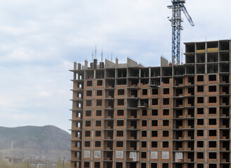 Fototapeta na wymiar Construction of a multi-storey monolithic-brick house. Construction high-rise crane. Window openings. Background - mountain, sky.