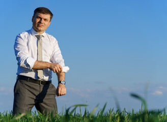businessman posing in a field, he rolls up his shirt sleeve, green grass and blue sky as background