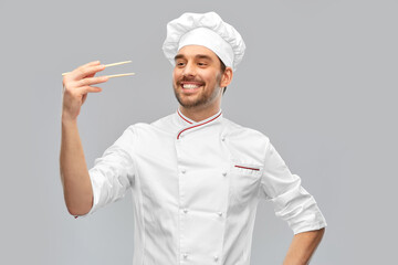 food cooking, asian cuisine and people concept - happy smiling male chef in toque holding something with chopsticks over grey background