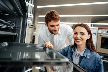 Fototapeta na wymiar Young couple choosing new electric oven in hypermarket