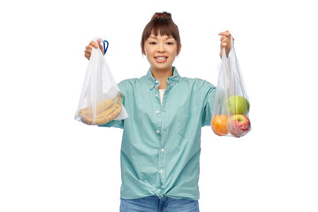 sustainability, eco living and people concept - portrait of happy smiling young asian woman holding reusable bag with bananas and plastic bag with apples over white background