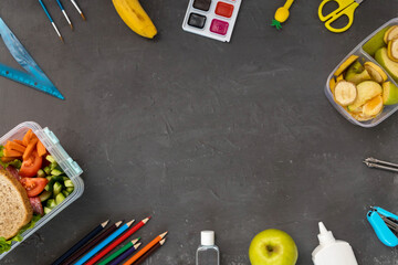 A school lunch box with a sandwich, vegetables, water and fruit on a gray concrete background. School supplies, stationery, and food. Flatly. From above. Copy space.