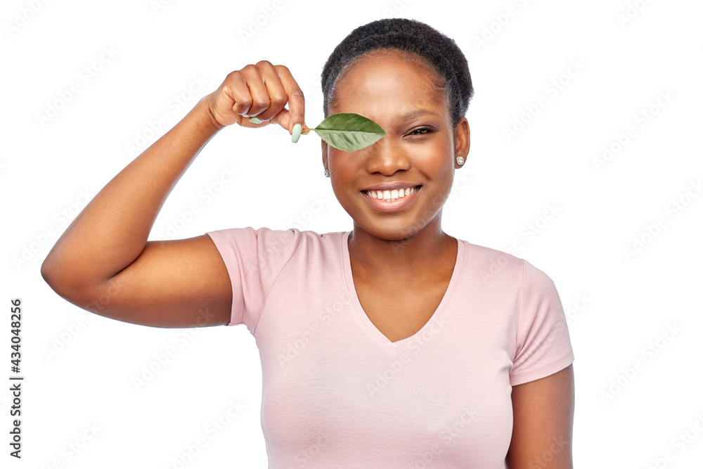 Wall mural eco living, environment and sustainability concept - portrait of happy smiling young african american woman covering one eye with green leaf over white background