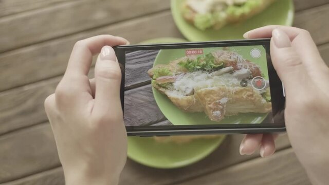Woman food blogger takes a photo on her smartphone of her breakfast with croissants. 
