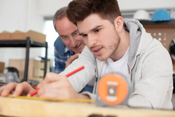 a carpenter and his apprentice marking a plank