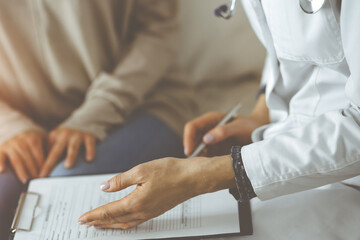 Close-up of woman-doctor and patient discussing current health examination while sitting indoors....