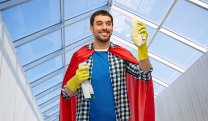 cleaning and people concept - happy smiling man in superhero cape and rubber gloves with rag and...