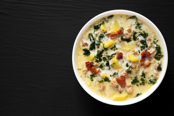Homemade Zuppa Toscana with Kale and Bread in a white bowl on a black background, top view. Overhead, from above. Copy space.