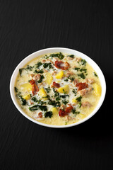 Homemade Zuppa Toscana with Kale and Bread in a white bowl on a black background, side view.