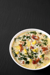 Homemade Zuppa Toscana with Kale and Bread in a white bowl on a black background, side view. Copy space.