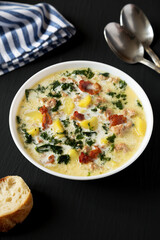 Homemade Zuppa Toscana with Kale and Bread in a white bowl on a black background, side view.
