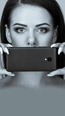 Portrait of attractive woman with bright makeup covering her mouth with smartphone. aspect ratio...