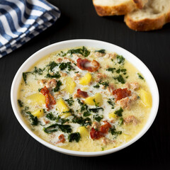 Homemade Zuppa Toscana with Kale and Bread in a white bowl on a black background, side view.