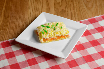 Russian traditional salad with vegetables and mayonnaise served on a white square plate over wooden table
