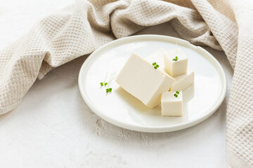 Pieces of tofu cheese with micro greens on a light plate with a linen towel.