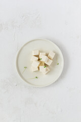 Pieces of tofu cheese with micro greens on a plate. Vertical orientation, top view.