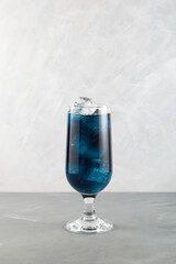 Close-up glass of blue lagoon cocktail. Tall glass of refreshing drink on light grey background. Vertical orientation, copy space