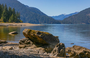 Beautiful landscape of the Harrison lake with large rocks in the foreground and mountains on the background.
