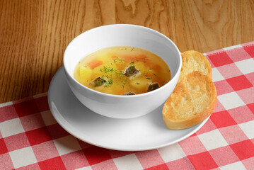 Chicken broth soup with vegetables served in a white bowl over red plaid tablecloth. Ukrainian cuisine concept.
