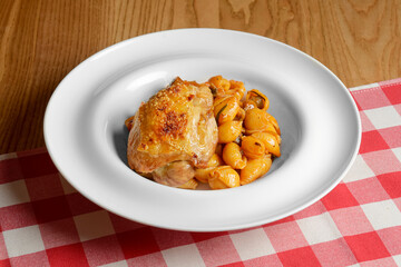 Plate of penne pasta with tomato sauce and meat. Served in a white plate over red plaid table cloth.