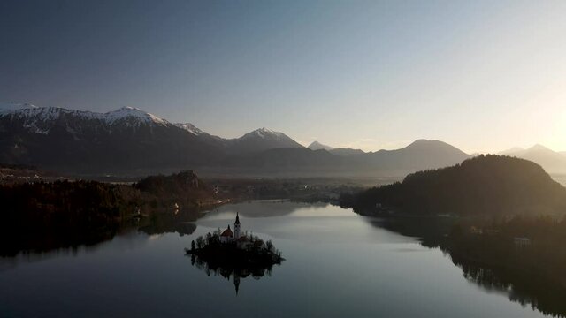 High flying aerial over Lake Bled, reflection of church islet against Alps mountains