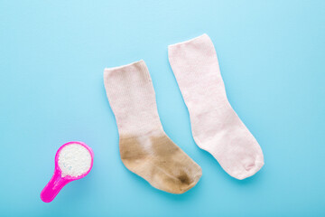 Baby socks and cup of white powder on light blue table background. Pastel color. Closeup. Detergent for clothes washing. Problem and solution. Compare dirty and clean socks. Top down view.