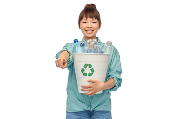 recycling, waste sorting and sustainability concept - smiling young asian woman holding rubbish bin with plastic bottles pointing finger to camera over white background