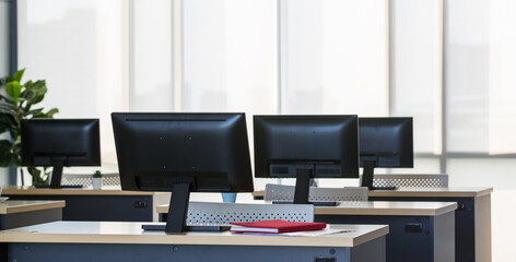 Background photo of modern indoor interior working space, office or workplace with nobody and row of computers on wooden desks or tables. Technology and Business Concept.